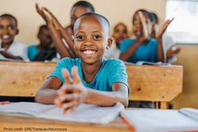 Girl sits smiling and clapping in classroom, Rwanda