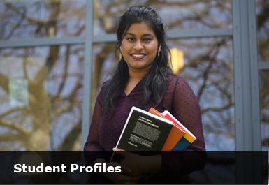a female postgraduate student stands in the faculty gardens outside the library holding a pile of books