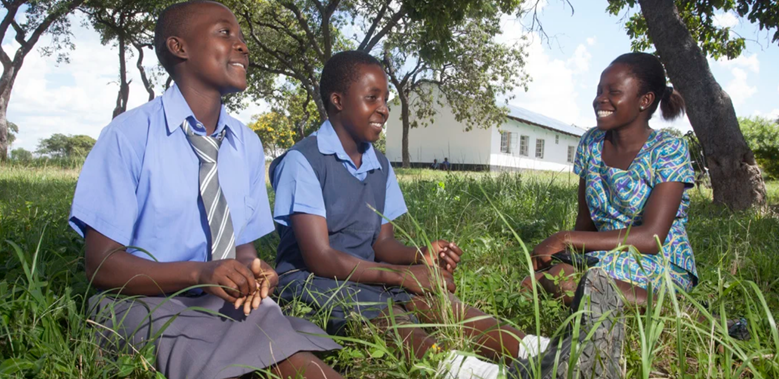Girls sit under a tree with their learner guide, Tanzania